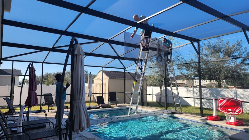 Technician on a ladder fitting new screen into the roof panels of a pool enclosure