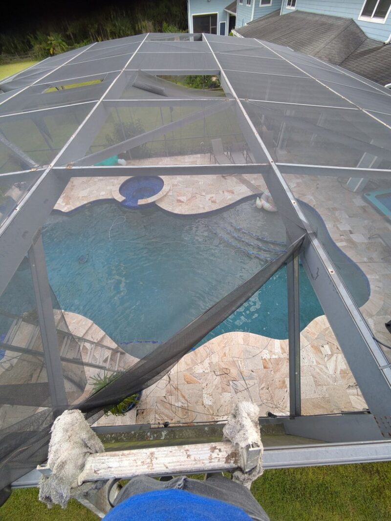 Overhead view of a pool cage part-way through a rescreen, several roof panels stripped back to bare frame