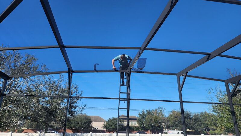 Technician working on a pool enclosure frame against a clear blue Florida sky